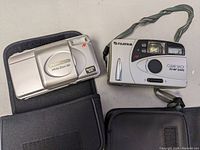 Both Olympus Infinity Zoom 80 and Fujifilm Clear Shot cameras side by side with black cases visible underneath.
