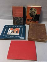 Five vintage books arranged on a white surface: The Time Machine by H.G. Wells, Trotsky, a book on reptiles of Ceylon, a blue softcover book titled Lobby Cards, and one more book.