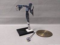 Art Deco figure sculpture on base with separate brass plate and metal rod with ball end, viewed from the side.
