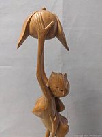 Front angle of the wooden sculpture showing the taller cat holding a round object with leaf-like extensions and the smaller cat climbing up.
