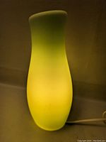 Photo of the green glass lamp lit, showing smooth, vase-like shape and yellow-green color.