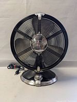 Front view of black Hunter table fan with metal grille and chrome center badge and base detailing.