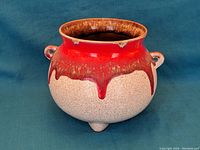 Front angled view of the bowl showing the red drip glaze over cream textured base and three small feet.