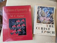 Front cover photo of two hardcover books, 'Visions of Symmetry' by Doris Schattschneider on M.C. Escher and 'The Cubist Epoch' by Douglas Cooper, showing cover art and titles.