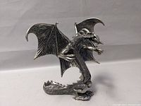 Front side view of the pewter winged dragon figure showing extended wings and detailed head with open mouth and claws.