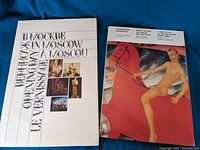 Two oversize art books with covers visible, one titled 'В Москве' In Moscow Le Vernissage and the other featuring a nude figure on horseback titled Born of the October Revolution.