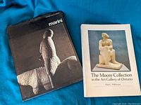 Two art books; one about Marino Marini sculpture with a black cover and one titled The Moore Collection in the Art Gallery of Ontario with a white cover showing a sculpture of a seated figure.