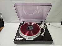 Full front view of turntable with red translucent vinyl on platter and purple-tinted dust cover open
