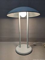 Full front view of the white UFO lamp showing round base, two vertical supports, and dome-shaped shade with light bulb inside.