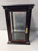 Front view of dark wood display cabinet with glass door and ornamental brass accents.