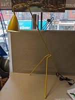 Full side view of the yellow metal floor lamp standing on a white surface near a window.