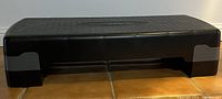 Black plastic exercise step platform shown from side view illustrating the height and structure.