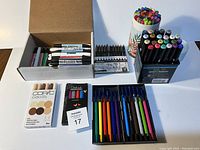 Photo showing five sets of art supplies: box of assorted markers, fineliners, colored pencils, Copic Ciao skin tone markers, and Chalkola metallic markers.