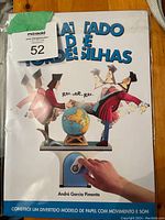 Front cover of the paper model kit shows cartoon figures, a globe, and a hand operating a lever to produce movement and sound. Title text in Portuguese.