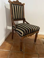 Full view of vintage Eastlake style occasional chair with vertical tan and black striped upholstery and carved wood frame.
