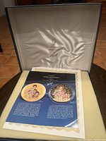 Closed original box with satin interior lining and certificate folder inside displaying plate series information and signatures.