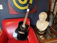 Full front view of black Ibanez guitar leaning on red chair with painting in background