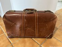 Front view of brown leather suitcase showing scratches, scuffs, and worn corners