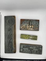 Top-down photo showing four printers blocks in varying shapes and sizes including an abstract design, industrial refinery scene, reversed text 'UNIVERSITY BOOKROOM', and a mechanical/abstract pattern.