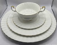 Stack of handled soup bowl on dessert, luncheon and dinner plates showing scalloped ridged edges and gold trim