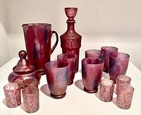 Overview of entire glass set including water pitcher, wine carafe, six water glasses, six shot glasses arranged on flat surface.