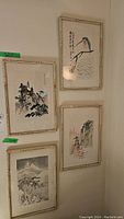 Four framed Asian art prints hung on a wall featuring landscapes and a bird, all with bamboo style light wood frames.