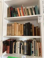 Books on three white shelves including poetry, collected works and classic literature.
