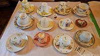 Overview of 12 assorted fine china teacups and saucers arranged on a table.