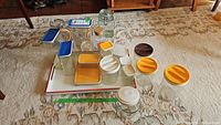 Overview of various glass containers and lids including yellow airlock lids, brown lids, white lids, and a cork stopper. Containers are of various sizes and shapes laid on carpet and tray.