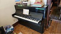 Black Yamaha upright piano against a wall with books and a CD player on the side.