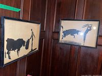 Both framed prints displayed on wood-paneled wall