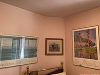 Three framed prints mounted above a brass bed headboard on peach wall