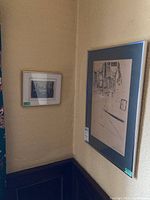Two framed prints on a wall corner showing a monochrome sketch art print in silver frame and a small colored landscape print in gold frame.