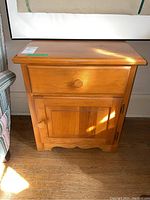 Full front view of wood side table showing drawer and cabinet door with round wooden knobs, natural wood finish, and scalloped base.