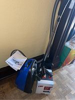 Blue Miele vacuum cleaner, manual, and accessories leaning against wall near wood floor