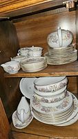Photo of stacked plates, teacups, and saucers inside wooden cabinet shelf