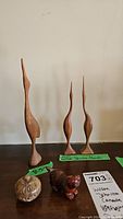 Three wooden bird carvings by Wilson Johnston with labels showing artist and origin (Canada), alongside a carved stone cat figure and a round trinket bowl with a geode inside on a wooden surface.