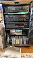 Full view of Yamaha stereo equipment setup including cassette deck, receiver, CD player stacked vertically with shelves of music CDs below. Yamaha FRX-500/U manual placed on floor in front.