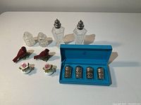 Full view of all shakers including sterling silver set in blue box, art deco glass shakers, cut crystal shakers, porcelain flower and bird shakers.