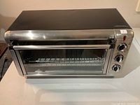 Front view of the BLACK+DECKER toaster oven showing stainless steel and black housing with handle and wire rack inside.