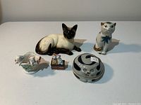 Photo showing entire assortment of five cat figurines including Siamese cat, tall painted cat, candy dish cat, and two small clustered cats on bases.