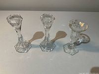 Set of three crystal candle holders on white surface, showing matching pair with cut geometric design and third floral holder at front