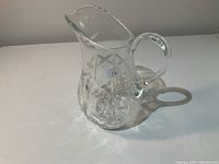 Front and side angle of clear antique crystal glass pitcher showing cut diamond and star patterns with handle and spout.