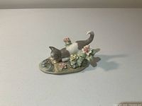 Full view of the Lladro porcelain figurine showing the kitten sniffing the frog with flowers around them.