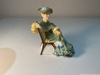 Side view of the Royal Doulton Ascot figurine showing seated lady in green dress with hat and closed parasol on chair