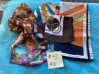 Four vintage scarves laid flat in a group showing varied colors and abstract patterns including brown, orange, multicolor, teal, and navy elements.