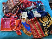 Overall view of six vintage silk scarves with various designs laid out on a blue surface.