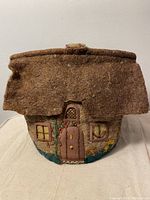Front view of the antique folk art tea cozy shaped like a cottage with detailed embroidery on the door and windows and flower motifs.