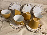 Full view of six cups and saucers arranged with cups both upright and resting on saucers showing colors and pattern detail.