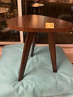 Full view of three-legged wooden side table with triangular wood grain finish top and tapered legs